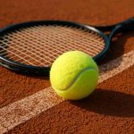 Tennis ball on clay court next to racket"