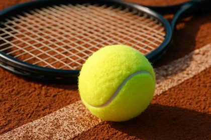 Tennis ball on clay court next to racket"