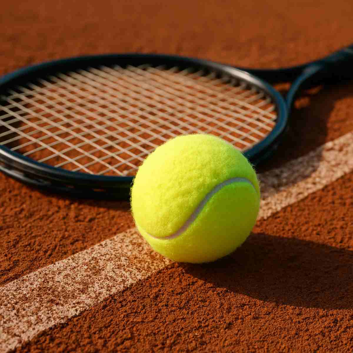 Tennis ball on clay court next to racket"