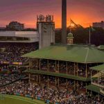 "Crowded cricket stadium with sunset sky in the background"
