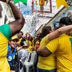 Crowd of Brazilian fans celebrating in the street wearing yellow jerseys during a festive event.