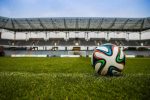 Soccer ball on green field inside an empty stadium"