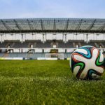 Soccer ball on green field inside an empty stadium"