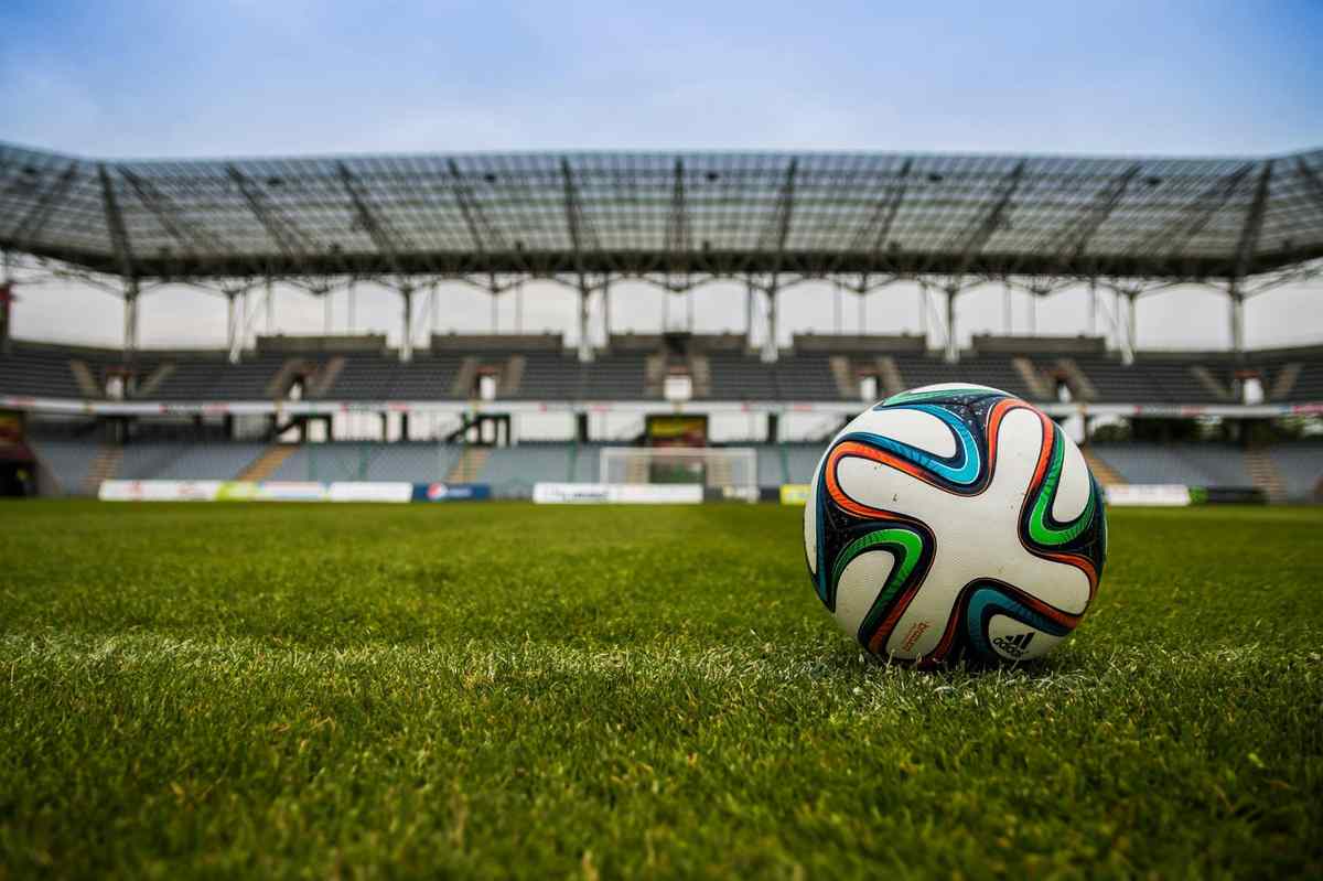 Soccer ball on green field inside an empty stadium"