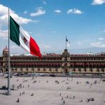 Mexican flag waving in Mexico City’s Zócalo square with the National Palace in the background.