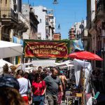 Crowd walking through San Telmo street market in Buenos Aires, Argentina, under colorful stalls and banners.