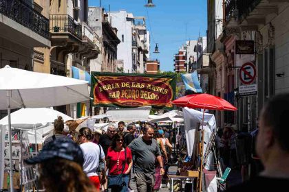 Crowd walking through San Telmo street market in Buenos Aires, Argentina, under colorful stalls and banners.