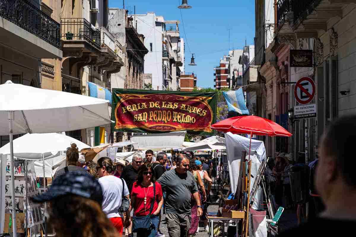 Crowd walking through San Telmo street market in Buenos Aires, Argentina, under colorful stalls and banners.