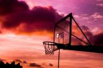 "Basketball hoop silhouette against a dramatic sunset sky with purple and orange clouds"