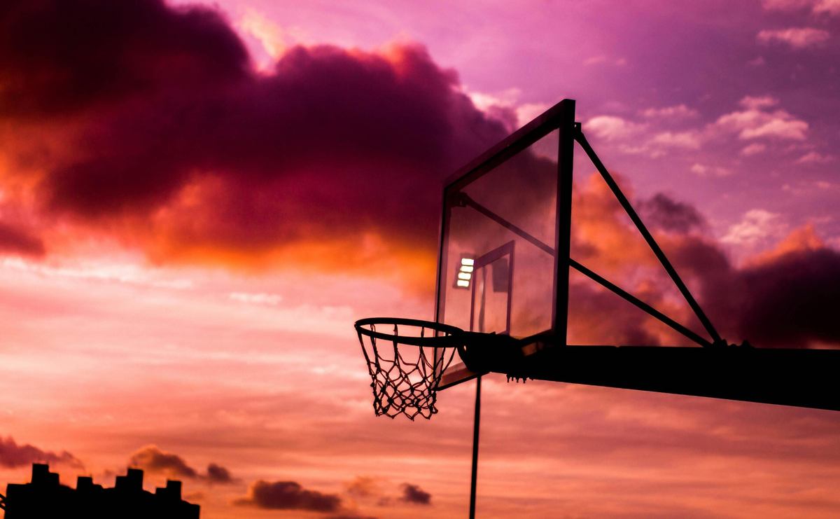 "Basketball hoop silhouette against a dramatic sunset sky with purple and orange clouds"