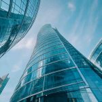 Upward view of a curved glass skyscraper reflecting the blue sky and nearby towers.