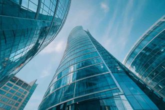 Upward view of a curved glass skyscraper reflecting the blue sky and nearby towers.
