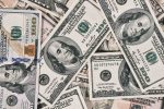 A close-up view of scattered US dollar bills showing $100 and $50 notes.