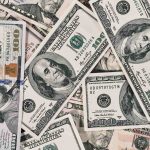 A close-up view of scattered US dollar bills showing $100 and $50 notes.