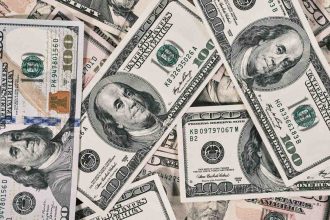 A close-up view of scattered US dollar bills showing $100 and $50 notes.