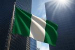 Nigerian flag waving in front of modern skyscrapers with sunlight shining through.