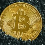Golden Bitcoin coin placed on a dark textured surface representing the rise of cryptocurrency value.