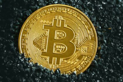 Golden Bitcoin coin placed on a dark textured surface representing the rise of cryptocurrency value.