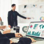 Professional team analyzing data charts on laptop dashboard during business meeting presentation.