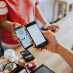 A person making a digital payment using a smartphone to scan a QR code at a café counter.