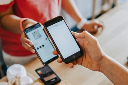 A person making a digital payment using a smartphone to scan a QR code at a café counter.