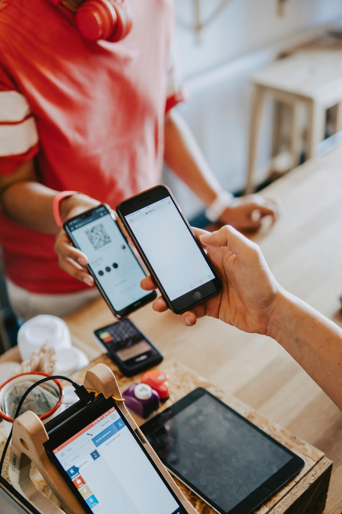A person making a digital payment using a smartphone to scan a QR code at a café counter.