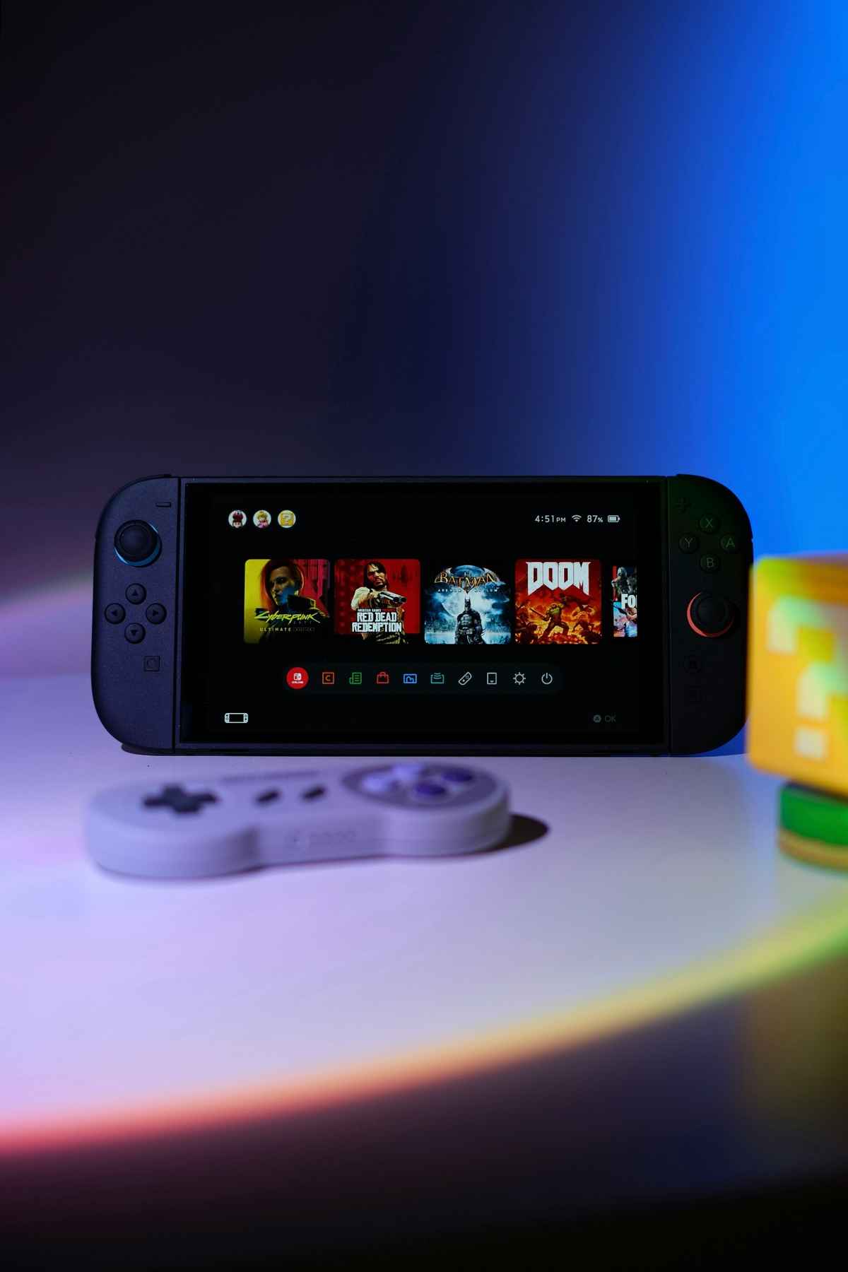 Nintendo Switch console with popular games on screen, accompanied by a retro controller and a Mario-themed cube under colorful lighting.