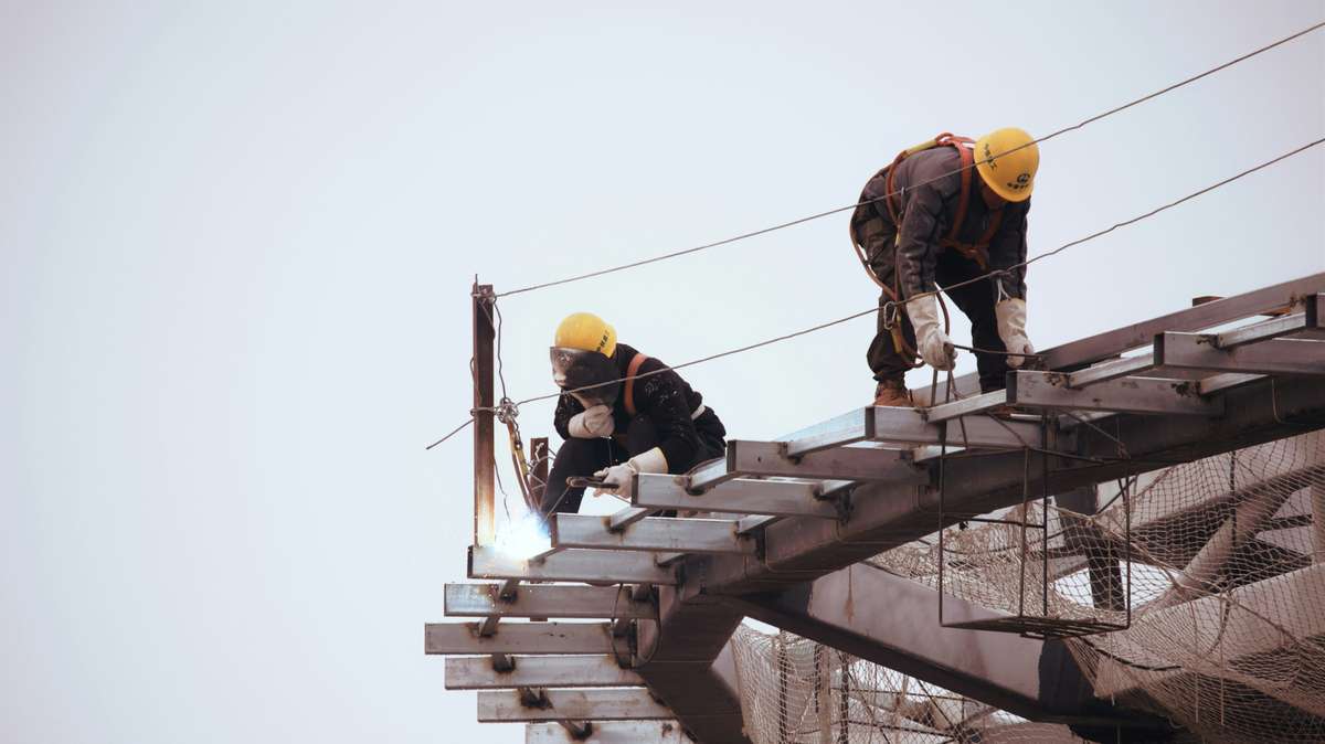 Construction workers welding and securing steel beams at a high-rise site.