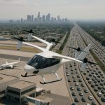 A sleek white eVTOL flying taxi hovers above a crowded city highway near an airport with airplanes on the tarmac and skyscrapers visible in the distance.