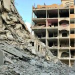 Destroyed residential building in Gaza after airstrikes, with rubble and collapsed concrete filling the street below.