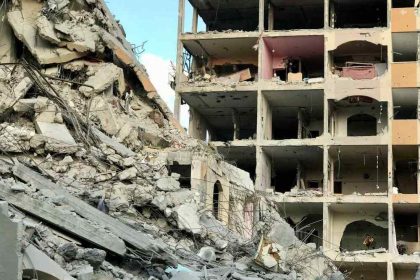 Destroyed residential building in Gaza after airstrikes, with rubble and collapsed concrete filling the street below.