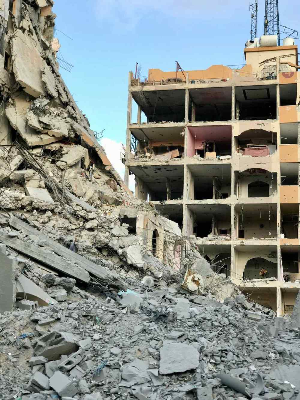 Destroyed residential building in Gaza after airstrikes, with rubble and collapsed concrete filling the street below.