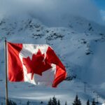 Canadian flag waving proudly against a snowy mountain backdrop under a bright sky.