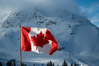 Canadian flag waving proudly against a snowy mountain backdrop under a bright sky.