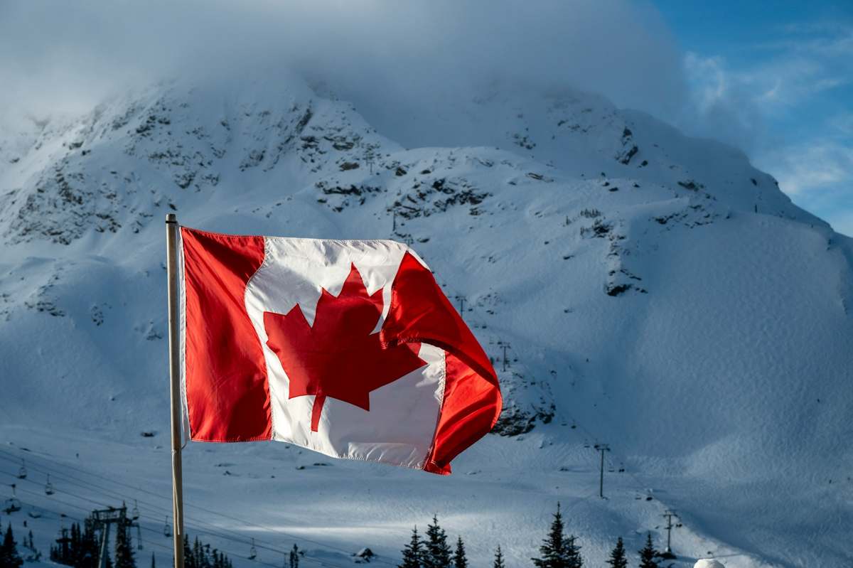Canadian flag waving proudly against a snowy mountain backdrop under a bright sky.