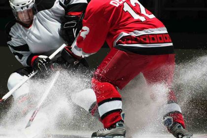Two ice hockey players in action during a competitive match, creating snow spray on the rink.
