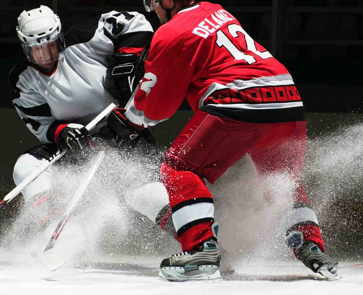Two ice hockey players in action during a competitive match, creating snow spray on the rink.