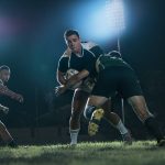 Rugby players in action during a night match under stadium floodlights.