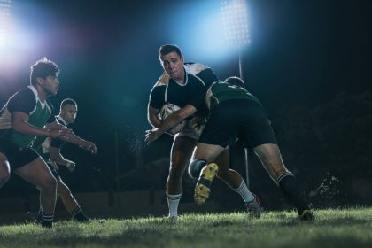 Rugby players in action during a night match under stadium floodlights.