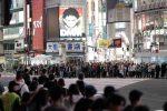 Crowds waiting at Shibuya Crossing in Tokyo at night with illuminated billboards.