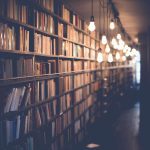 Rows of books on shelves in a library with hanging light bulbs.