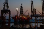 Offshore oil rig illuminated at dusk with cranes and lights reflecting on the calm sea