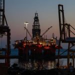 Offshore oil rig illuminated at dusk with cranes and lights reflecting on the calm sea