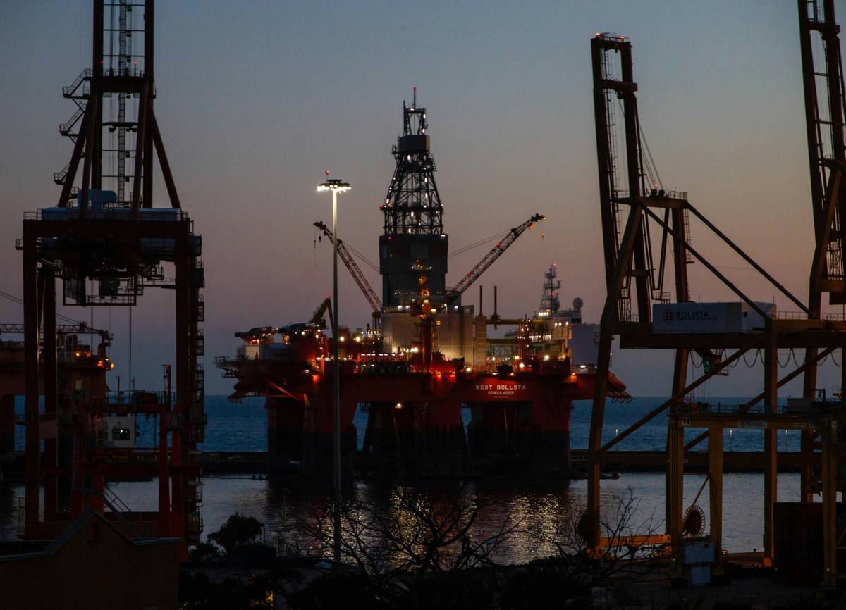 Offshore oil rig illuminated at dusk with cranes and lights reflecting on the calm sea