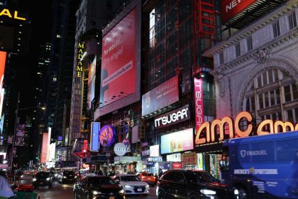 AMC Theatres sign glowing at night on a busy city street in Times Square with cars and neon billboards.