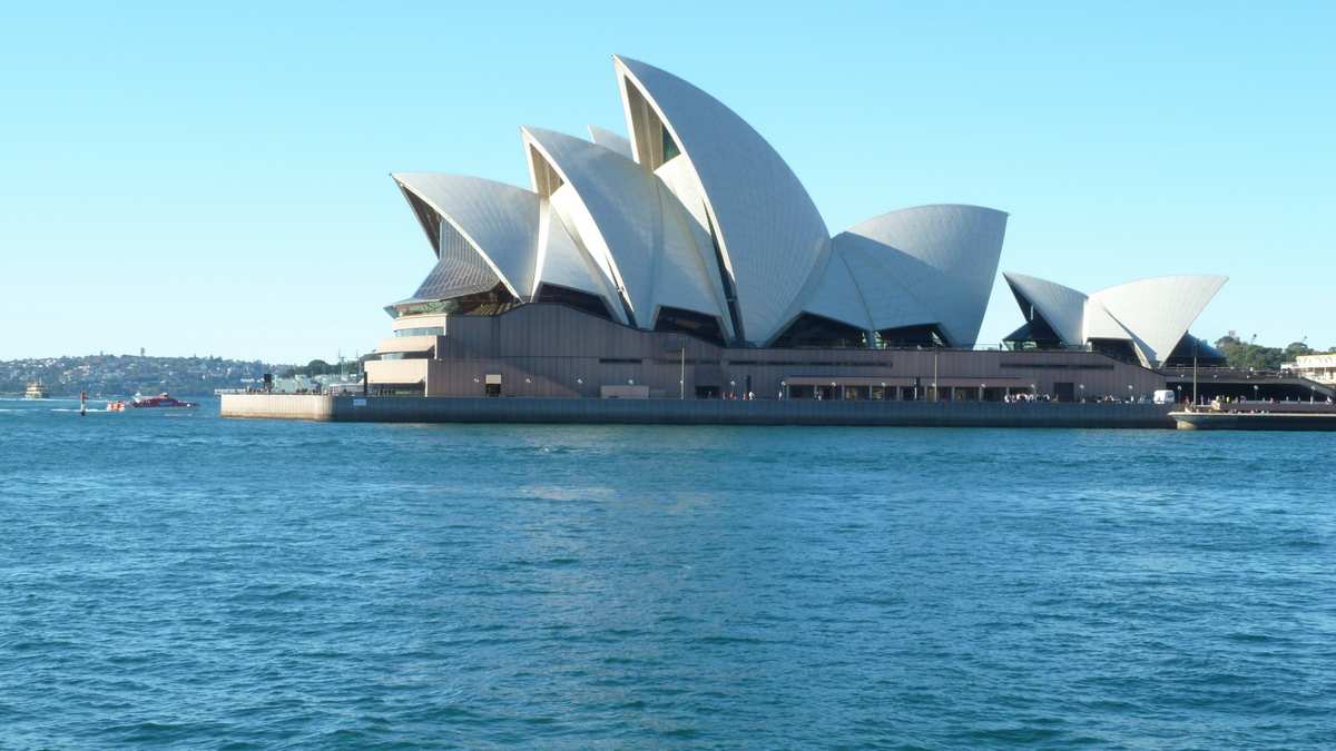 Sydney Opera House viewed from the harbor with clear blue skies.