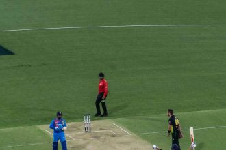 Indian cricket player celebrating a victory on the pitch during an international match under stadium lights.