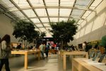 Customers inside a modern Apple Store with wooden tables and electronic devices.
