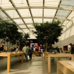 Customers inside a modern Apple Store with wooden tables and electronic devices.