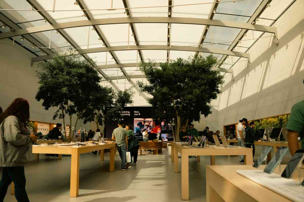 Customers inside a modern Apple Store with wooden tables and electronic devices.